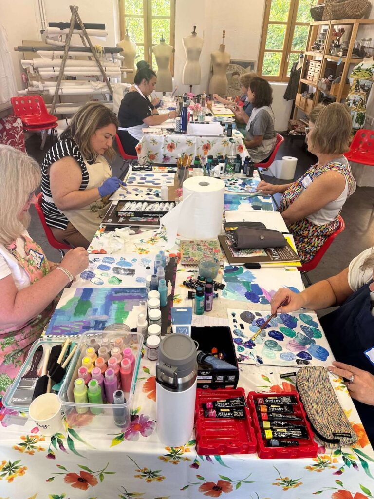 Kelly Rae Roberts retreat participants painting at a long table.